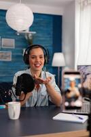 Woman vlogger recording live stream podcast on smartphone. Influencer talking in front of mobile phone camera and filming for social media channel, using microphone and headphones. photo