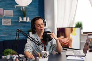 Content creator touching microphone to test sound. Vlogger testing audio equipment with finger. Woman influencer with headphones in home studio doing sound check for online podcast. photo