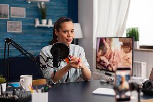 Content creator streaming makeup review for social media channel. Popular influencer recording product recommendation with smartphone and microphone for vlog in home studio. photo