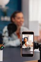 Closeup of smartphone recording white box review. Mobile phone filming smiling influencer doing product recommendation. Social media online podcast in home recording studio with microphone. photo