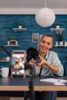 Content creator filming mouse review with mobile phone. Woman influencer in home studio with microphone and smartphone recording product testing. Online vlog podcast for social media. photo