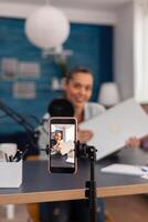 Closeup of smartphone recording product review. Mobile phone filming woman presenter doing vlog testing of laptop computer. Social media influencer doing gadget recommendation in front of camera. photo