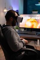 Person wearing vr glasses to play games with controller on computer. Man losing game with virtual reality goggles and joystick in front of monitor. Gamer playing game. photo