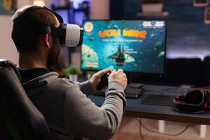 Adult using vr goggles to win games on computer. Man with controller and virtual reality glasses playing game to have fun with modern activity. Gamer winning online competition photo
