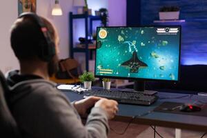 Man playing games with controller and headphones on computer. Player using joystick and audio headset for online gaming. Gamer having fun activity with equipment to play games. photo