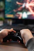 Close up of gamer holding controller to play games in front of computer. Player using joystick and playing online games on monitor, sitting at desk. Man gaming with modern equipment. photo