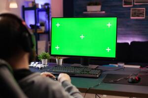 Gamer using horizontal green screen on computer. Man playing games on chroma key with isolated mockup template and background on display. Player with technology and equipment. photo