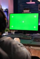 Close up of man using horizontal green screen on computer. Adult playing games on chroma key with isolated mockup template and background on display. Gamer with technology and equipment. photo