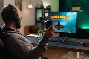 Player winning games with controller and headset in front of monitor. Man using joystick and headphones, playing online games on computer. Person celebrating game win for leisure. photo