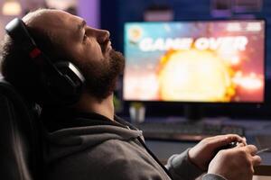 Man feeling disapointed about losing games on computer. Gamer with headphones using controller and playing online games on monitor. Sad player lost cyber game competition. photo