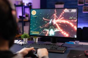 Man playing games with joystick on computer. Player using controller and wearing headphones to play online game on monitor. Modern person using gaming equipment to have fun. photo