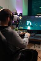 Person using vr goggles and joystick to play games. Man with virtual reality headset holding controller in front of computer, playing online game. Player having fun with games. photo