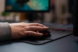 Close up of gamer holding mouse on mousepad to play games. Man using gaming equipment on computer, playing online game at desk. Hand of player on gadget having fun with games photo