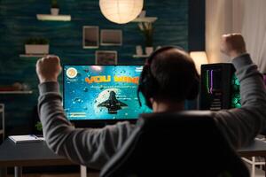 Man raising hands after winning games on computer. Person playing online games with monitor and headphones, celebrating win and feeling happy. Player with gaming technology photo