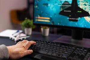 Close up of man using keyboard to play games on computer. Gamer playing online games on monitor with keypad, having modern gaming equipment. Player using control gadget. photo