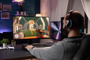 Adult with headphones playing games on computer. Man wearing headset, using keyboard and mousepad to play online game on monitor with gaming equipment. Modern player photo
