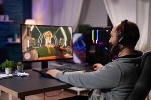Gamer with headset playing games on computer. Man wearing headphones, using keyboard and mousepad to play online game on monitor with gaming equipment. Modern player photo