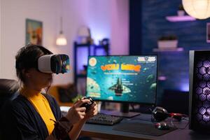 Woman winning games with vr glasses on computer. Gamer playing with virtual reality headset and controller to win online game on monitor. Player with modern equipment at desk. photo