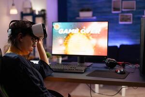Gamer using vr goggles to play games and losing on computer. Person playing online game with controller on monitor and virtual reality glasses. Adult with gaming equipment. photo
