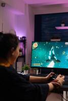 Gamer playing games with joystick on monitor. Cheerful woman using controller to play online game on internet. Player doing fun activity in cyber space with gaming equipment. photo