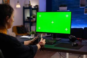 Woman looking at horizontal green screen on monitor, playing games with controller. Gamer using chroma key with isolated background and mockup template on computer display. photo