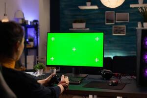 Player using horizontal green screen on computer, playing games with controller. Woman looking at chroma key with isolated background and mockup template on monitor display. photo