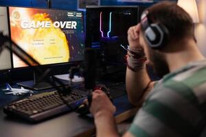 Adult playing games on live stream with chat and losing. Man using headphones and microphone to broadcast gameplay, streaming lost game on computer. Gamer live streaming online. photo