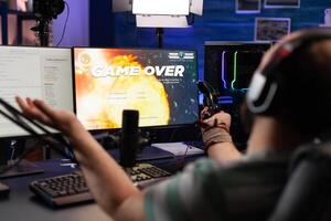 Player streaming games with headset and losing on computer. Man looking at monitors with live stream chat and online game, playing and broadcasting gameplay with microphone. photo