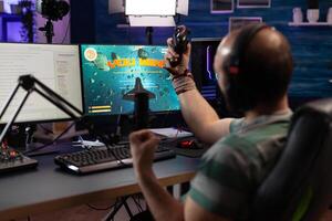Man winning games and live streaming on computer. Adult showing online gameplay on live stream with chat while he uses controller, headphones and microphone. Streamer broadcasting photo