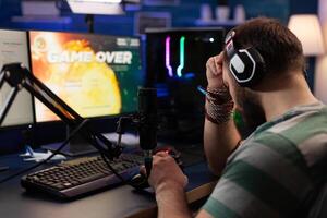 Man losing games and streaming with live chat on computer. Person showing gameplay on online stream with microphone and headphones. Player live streaming digital games on monitor. photo