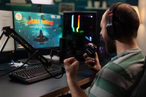 Streamer winning games with joystick on computer. Man live streaming gameplay and celebrating win, using microphone and headphones while he talks to online chat on monitor. Gamer on stream photo