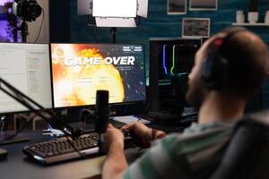 Man streaming games with microphone and losing on computer. Gamer looking at monitors with live stream chat and online game, playing and broadcasting gameplay with headphones. photo