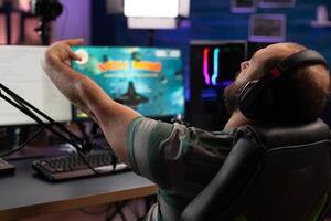 Gamer celebrating gameplay win with live chat on stream. Man streaming and playing games on computer with microphone and headset. Player winning game while he is live streaming. photo