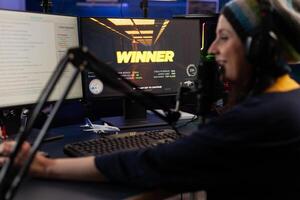 Woman live streaming online games on computer. Person broadcasting gameplay, playing live on stream with chat, using monitor and microphone. Streamer wearing headphones to play. photo