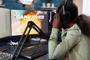 Sad upset pro gamer woman playing space shooter games losing online championship while talking with players on streaming chat. Nervous streamer using RGB gaming computer. Game over on screen photo
