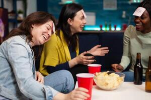 Laughing multi-ethnic friends playing who i am game using stickey notes enjoying spending time together during wekeend party at home. Group of people drinking beer guessing correct answer photo