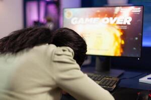 Sad loser gamer person playing space shooter games losing online championship. Nervous african american player using RGB computer equipment sitting in gaming home studio. Esports tournament photo