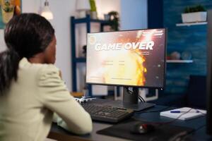 Upset pro gamer woman playing space shooter videogames losing online championship. Nervous african american player using RGB computer equipment sitting in gaming home studio. Esports tournament photo