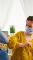 Cheerful african woman and her friend touching elbow keeping social distancing while greating each other wearing face mask, to prevent coronavirus spread in the course of global pandemic in living room photo