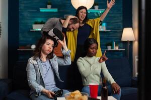 Upset sad woman wearing virtual reality headset holding gaming joystick playing videogames losing online competition. Group of multi-ethnic friends enjoying hanging out together making fun activity photo