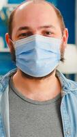 Portrait of man putting on protection mask looking at camera spending good time with friends in living room respecting social distance in global pandemic. People socializing during covid 19 outbreak photo
