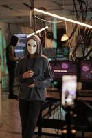 Online criminal in mask recording , asking victim for money, internet fraud, cyber scam, anonymous threatening on phone camera. Cybercrime, hacker stealing information, hacking computer system photo