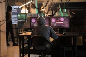 Cybercrime, internet thief hacking computer system, stealing data. Hacker sending virus, breaking into database server, coding spyware, programming malicious software, back view photo