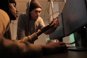 Internet criminals discussing computer system hacking, cyberattack. Hackers in hoodies coding password cracking pogram, scammers programming malicious software at night time photo