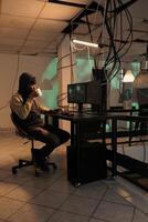 Young man working on security breach hacking, committing cyberterrorism and stealing personal data. causing computer malware at night. Online criminal cracking server encryption. photo