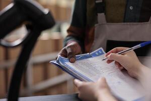 Warehouse manager signing cargo checklist, discussing merchandise inventory working at goods quality control. Diverse team preparing customers orders for delivery in storehouse. Close up photo