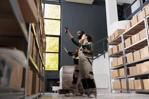 Stockroom colleagues working at merchandise inventory, scanning cardboard boxes using store scanner. Manager with supervisor working at clients orders, preparing packages for delivery in storehouse photo
