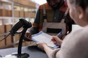 Diverse team analyzing merchandise checklist signing report in warehouse, discussing products quality control. African american employee wearing industrial overall, working at clients orders. Close up photo
