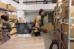 Storage room manager preparing orders and checking parcels in stockroom. African american employee using adhesive tape on cardboard boxes before shipping to clients in delivery company photo