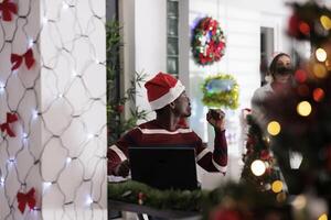 Worker tasked with stressful job duties bothered by background noise made by coworkers laughing while enjoying Christmas holiday season. Employee working on laptop, surrounded by in xmas ornaments photo